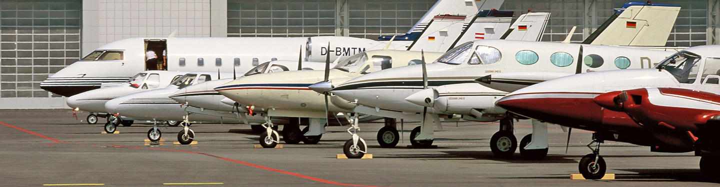 General Aviation Reihe kleiner Geschäfts- und Privatflugzeuge, darunter Jets und zweimotorige Propellermaschinen, die dicht nebeneinander auf dem Vorfeld des Flughafens München geparkt sind. Die Szene wirkt ruhig und technisch geprägt.