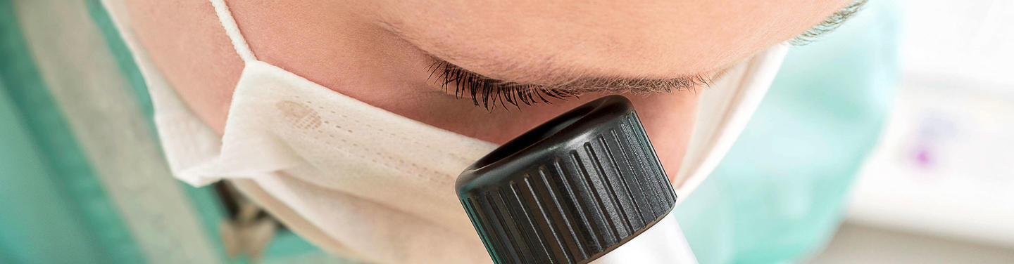 Hautärztliche Untersuchung am Flughafen München Nahaufnahme eines Hautarztes mit Mundschutz, der durch ein Untersuchungsgerät auf die Haut blickt, während eine dermatologische Kontrolle am Flughafen München durchgeführt wird; die Atmosphäre wirkt hygienisch, ruhig und sorgfältig.