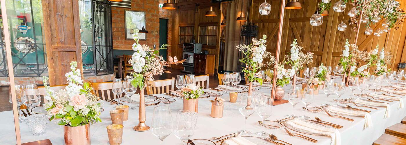 Airbräu Tenne Airbräu TenneLange festliche Tafel mit weißen Tischdecken, feinen Gläsern und floralen Arrangements in zarten Farben. Das stilvolle Ambiente eignet sich perfekt für Hochzeiten und Firmenfeiern.