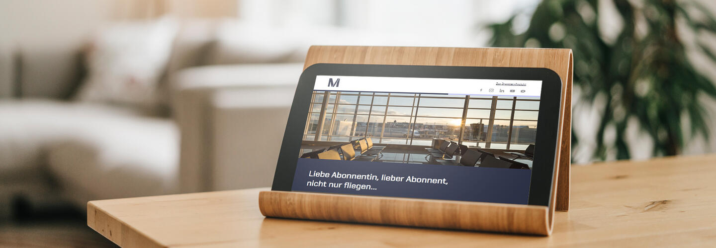 Newsletter Ein Tablet auf einem Holztisch zeigt die Website des Flughafens München. Die moderne Darstellung unterstreicht digitale Services, Online-Buchungen und kundenfreundliche digitale Angebote.