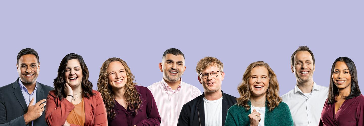 9.000 Mitarbeitende - ein Arbeitgeber - grenzenlose Jobvielfalt Gruppenfoto von acht freundlich lächelnden Mitarbeiter und Mitarbeiterinnen in unterschiedlicher Kleidung vor einem hellvioletten Hintergrund.