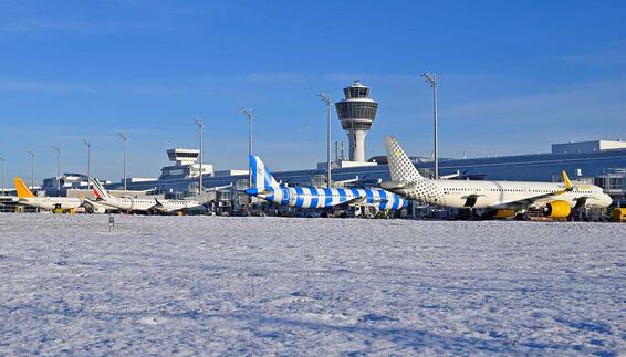 Schnee auf dem Vorfeld Verschneites Vorfeld am Flughafen München mit mehreren geparkten Passagierflugzeugen und dem Tower im Hintergrund an einem klaren Wintertag.