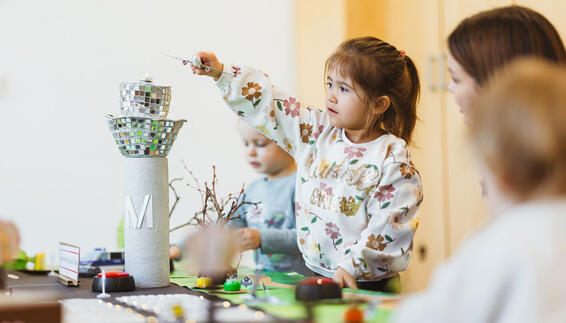 Airport Hopser Kinder spielen an einem gebastelten Flughafenmodell, während ein Kind ein kleines Flugzeug über den Tower hält.
