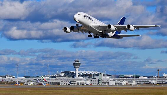 Lufthansa Airbus A380-800 Lufthansa Airbus A380-800 beim Start über dem Flughafen München mit Terminalgebäuden und Tower im Hintergrund.